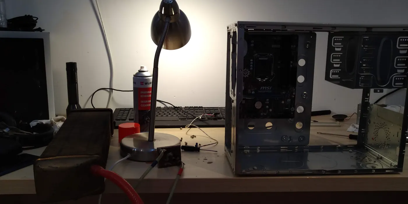 Pusta obudowa komputera z płytą MSI na biurku, obok lampka, puszka czyściwa i radiator z czerwonym wężem