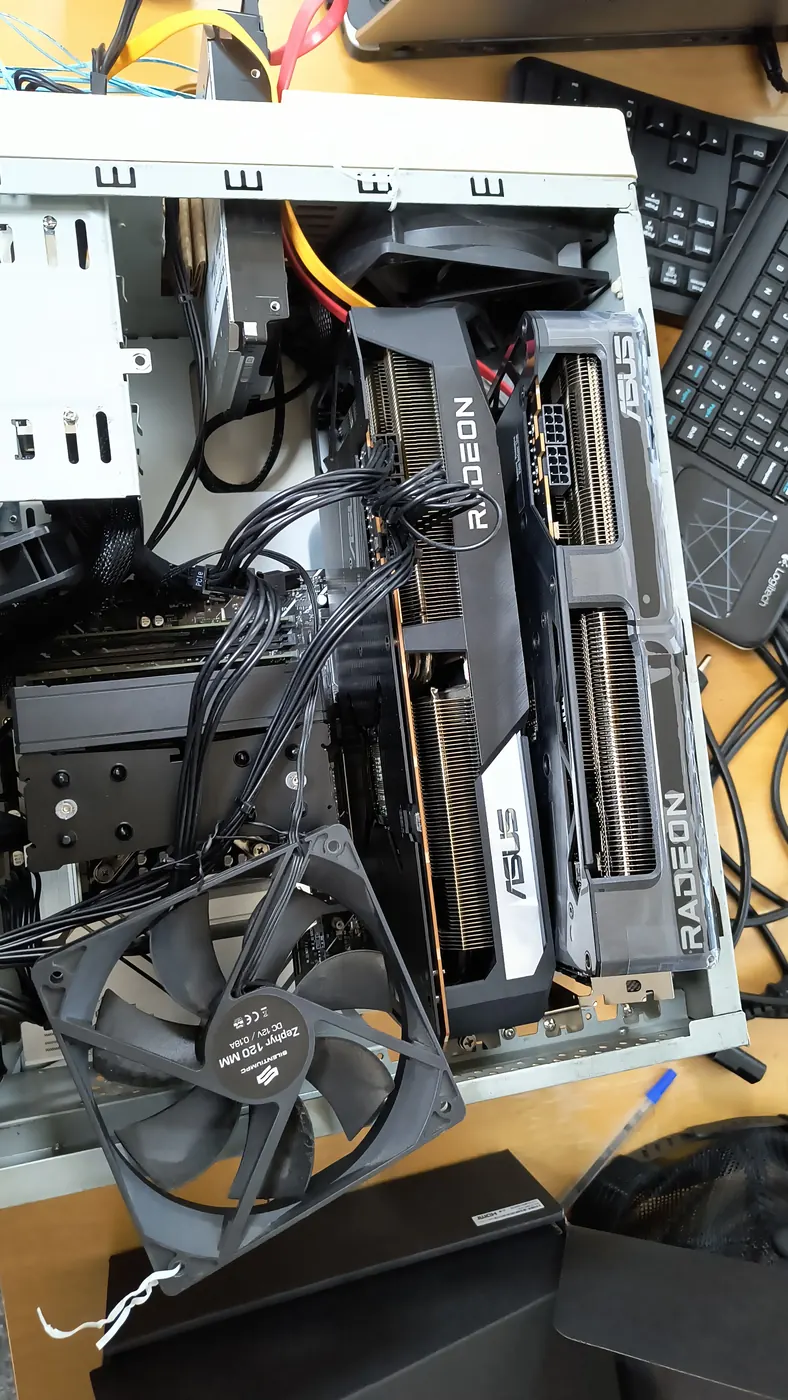 Dwie karty graficzne Radeon obok siebie w otwartej obudowie, na wierzchu luźny wentylator